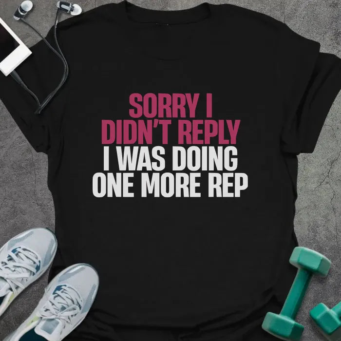 Black t-shirt printed with "Sorry I Didn't Reply I Was Doing One More Rep" in white and pink