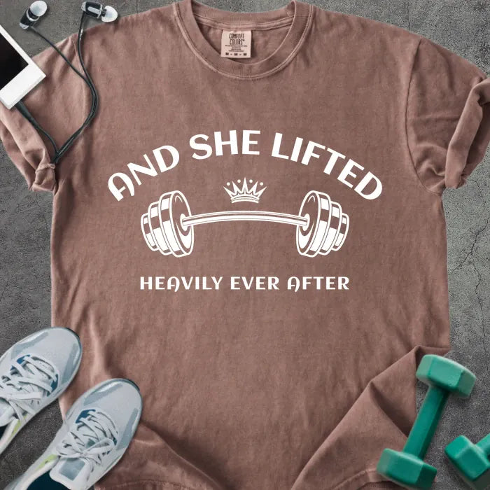 Espresso t-shirt printed with "And She Lifted Heavily Ever After" in white, with a barbell and crown