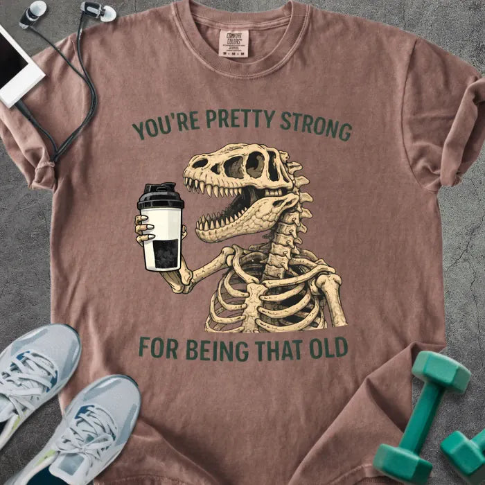 Espresso t-shirt printed with "You're Pretty Strong for Being That Old" in green, with skeleton holding a coffee cup