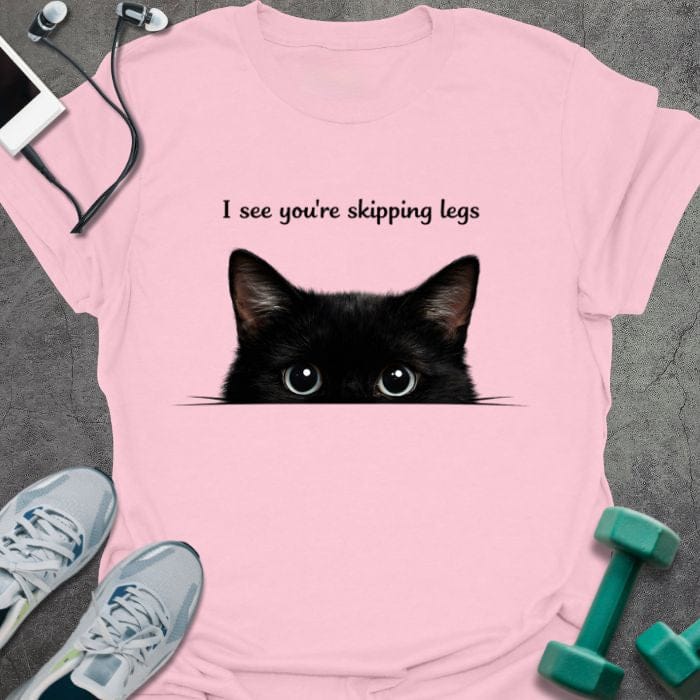Light pink t-shirt printed with "I see you're skipping legs", with a black cat peeking over the bottom edge of the text