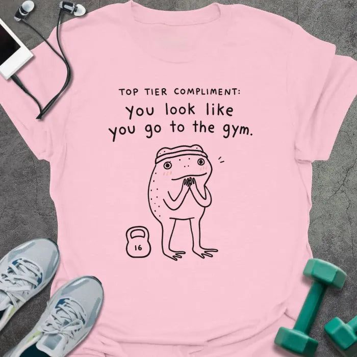 Light Pink t-shirt printed with "TOP TIER COMPLIMENT: you look like you go to the gym." in black, with frog graphic holding barbells