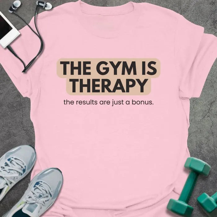 Light pink t-shirt printed with "THE GYM IS THERAPY the results are just a bonus." in black and gray