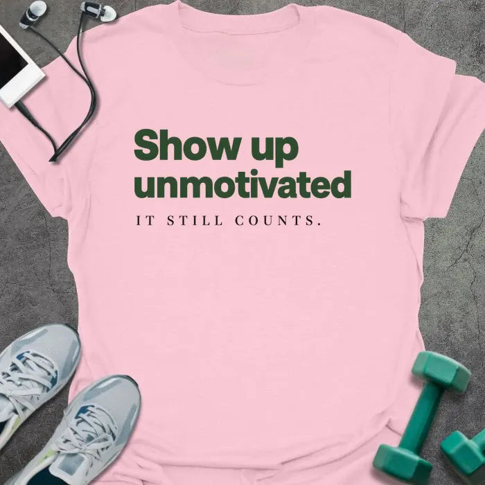 Light pink t-shirt printed with "Show up unmotivated IT STILL COUNTS." in green and black
