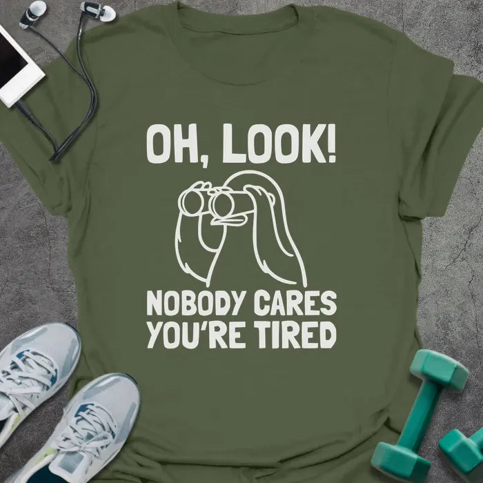 Military green t-shirt printed with "Oh, Look! Nobody Cares You're Tired", with an illustration of a person with binoculars