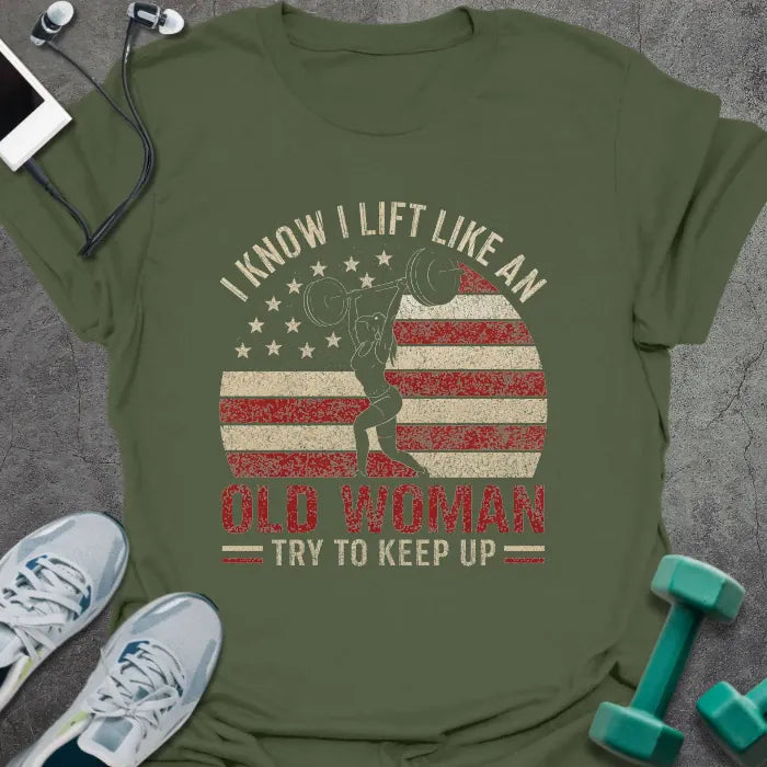 Military green t-shirt printed with "I Know I Lift Like an Old Woman Try to Keep Up" in red and white, with a flexing woman silhouette and American flag kettlebell
