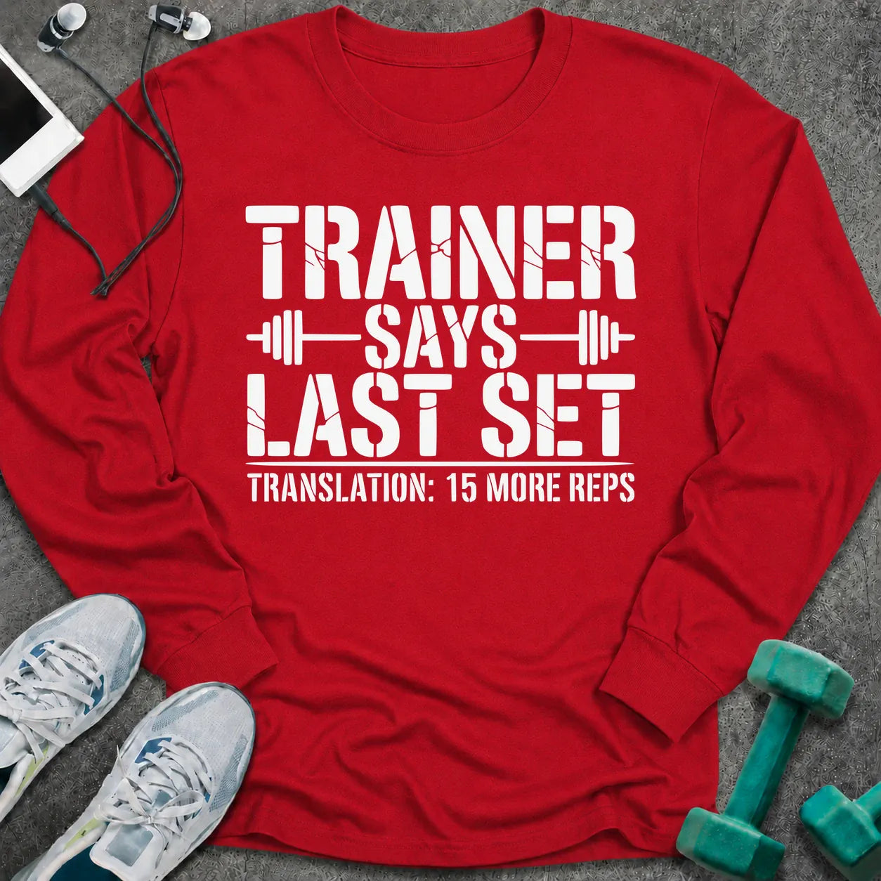 Red long sleeve tee printed with "Trainer Says Last Set. Translation: 15 More Reps" in white, with barbell accents