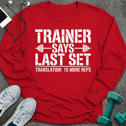 Red long sleeve tee printed with "Trainer Says Last Set. Translation: 15 More Reps" in white, with barbell accents