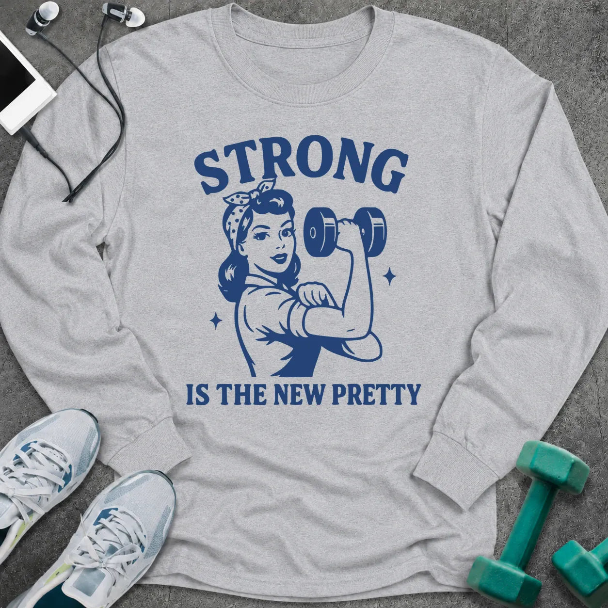 Ash long sleeve tee printed with "Strong Is The New Pretty" in navy, with a retro woman flexing with a dumbbell