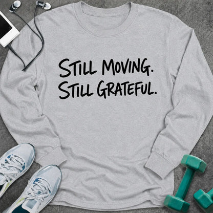 Ash long sleeve tee printed with "Still Moving. Still Grateful." in black handwritten lettering