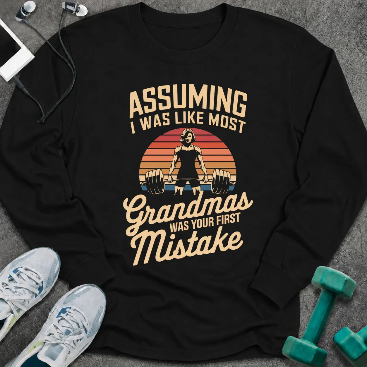 Black long sleeve tee printed with "Assuming I Was Like Most Grandmas Was Your First Mistake" in cream and gold, with a woman deadlifting inside a retro sunburst