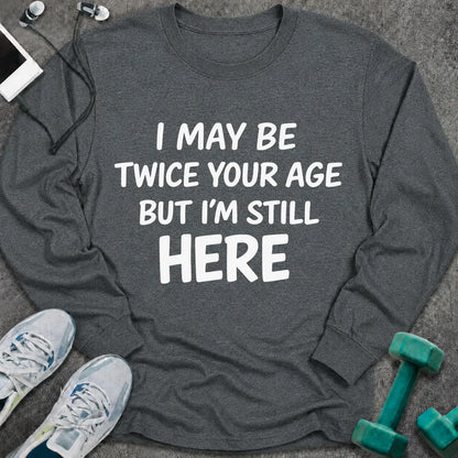 Dark heather long sleeve tee printed with "I May Be Twice Your Age But I'm Still Here" in white