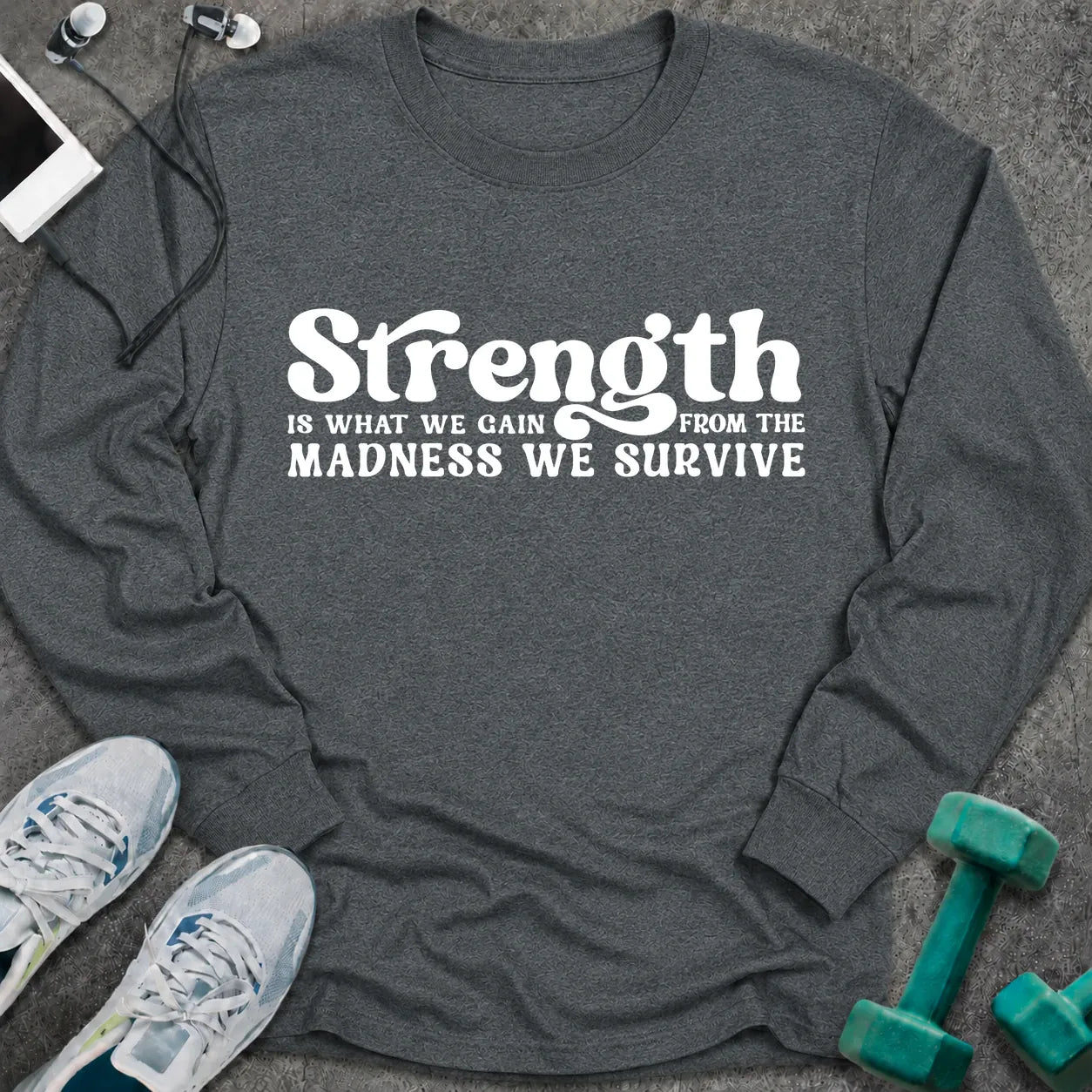 Dark heather long sleeve tee printed with "Strength Is What We Gain From The Madness We Survive" in white