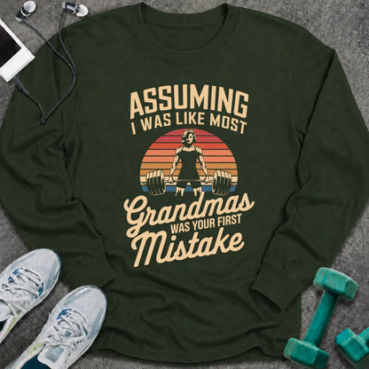 Forest green long sleeve tee printed with "Assuming I Was Like Most Grandmas Was Your First Mistake" in cream and gold, with a woman deadlifting inside a retro sunburst