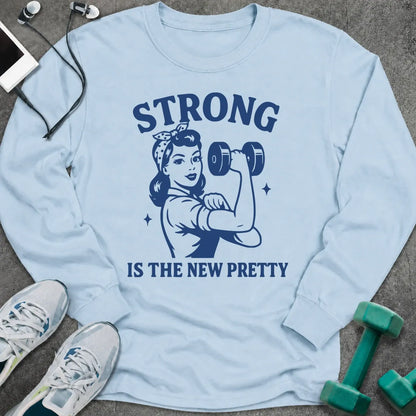Light blue long sleeve tee printed with "Strong Is The New Pretty" in navy, with a retro woman flexing with a dumbbell