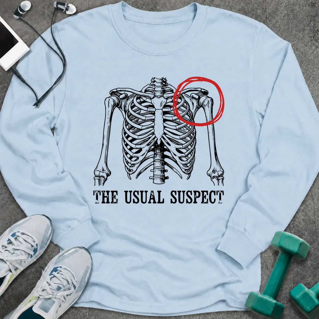 Light blue long sleeve tee printed with "The Usual Suspect" in black, with a skeleton ribcage with one shoulder circled in red