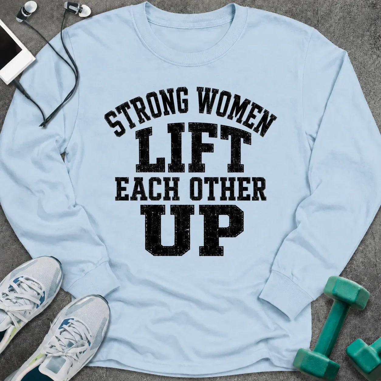 Light blue long sleeve tee printed with "Strong Women Lift Each Other Up" in black distressed varsity lettering