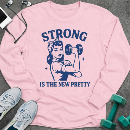 Light pink long sleeve tee printed with "Strong Is The New Pretty" in navy, with a retro woman flexing with a dumbbell