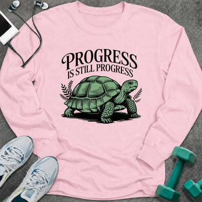Light pink long sleeve tee printed with "Progress Is Still Progress" in black, with a tortoise