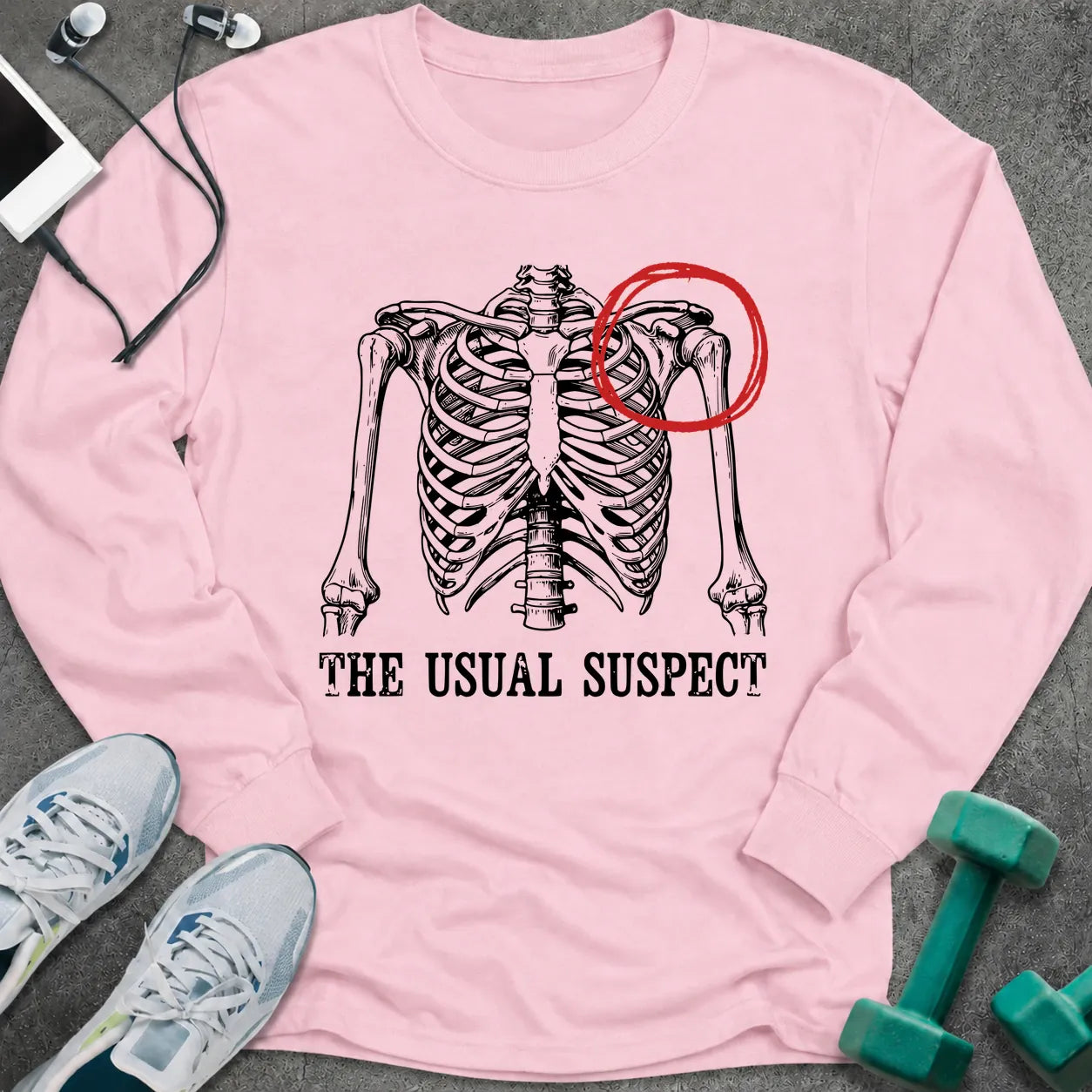 Light pink long sleeve tee printed with "The Usual Suspect" in black, with a skeleton ribcage with one shoulder circled in red