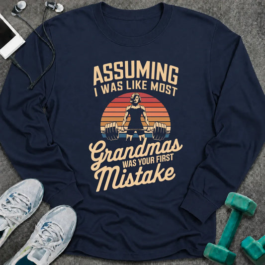 Navy long sleeve tee printed with "Assuming I Was Like Most Grandmas Was Your First Mistake" in cream and gold, with a woman deadlifting inside a retro sunburst