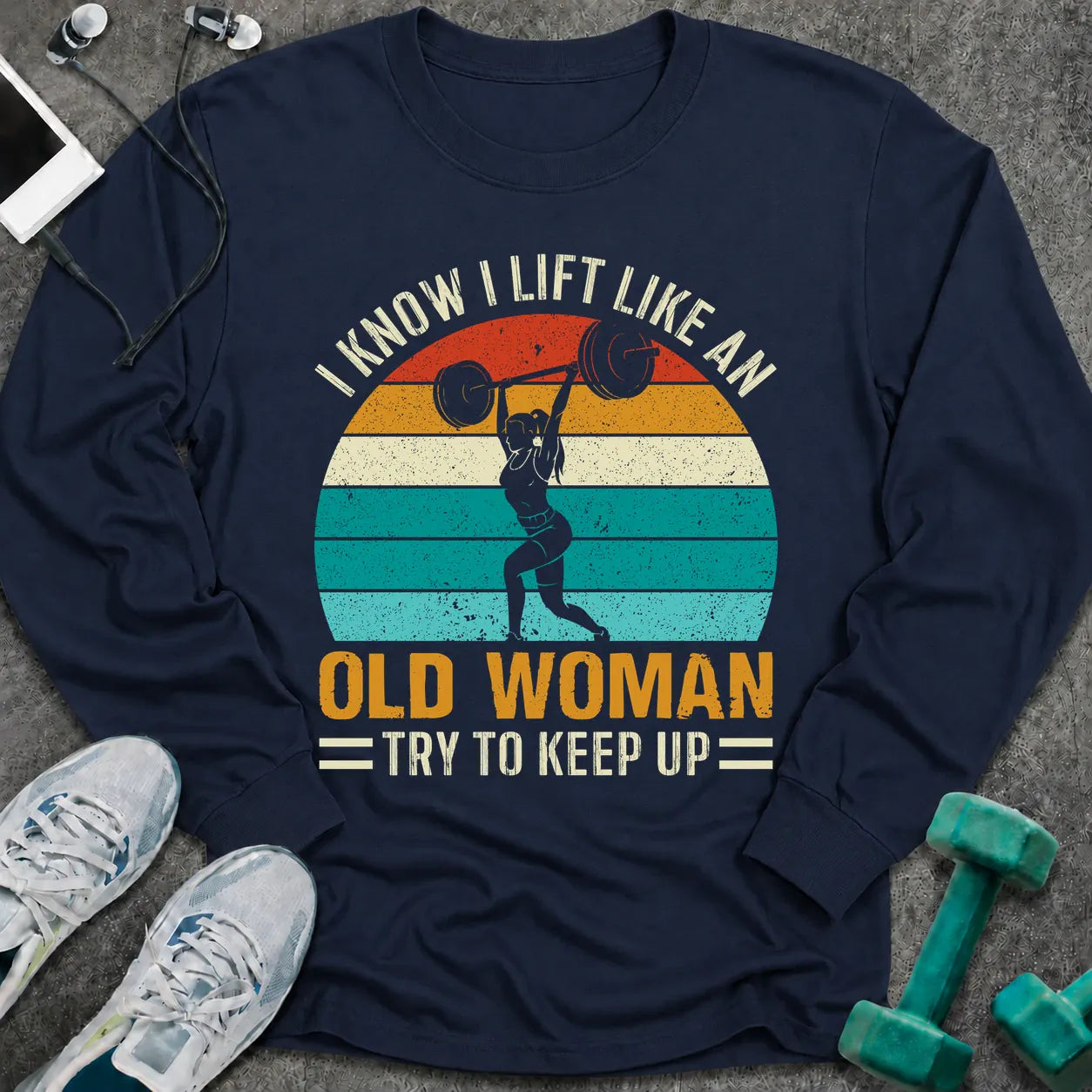 Navy long sleeve tee printed with "I Know I Lift Like An Old Woman, Try To Keep Up" in white and gold, with a woman pressing a barbell over a retro striped sunset