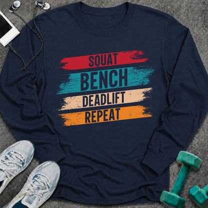 Navy long sleeve tee printed with "Squat Bench Deadlift Repeat" in white, with teal, cream and orange brush strokes behind each word