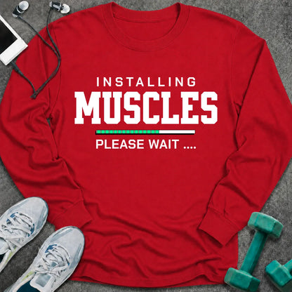 Red long sleeve tee printed with "Installing Muscles Please Wait" in white, with a green loading bar