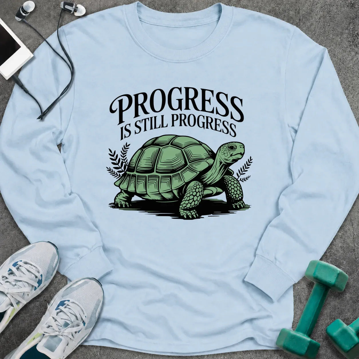 Light blue long sleeve tee printed with "Progress Is Still Progress" in black, with a tortoise