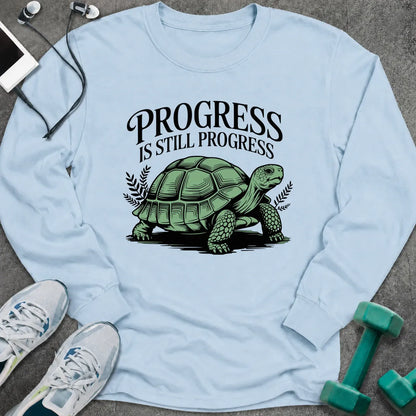 Light blue long sleeve tee printed with "Progress Is Still Progress" in black, with a tortoise