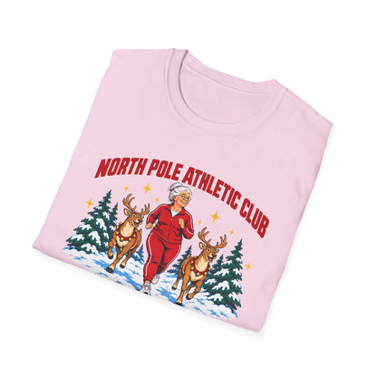 Folded light pink t-shirt printed with "NORTH POLE ATHLETIC CLUB" in red and "Winter Training Season" in green script, with a white-haired woman in a red tracksuit jogging between two reindeer through snowy pine trees