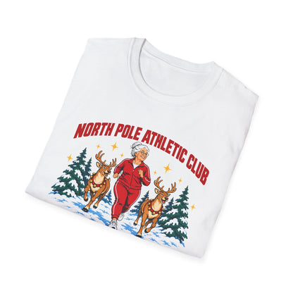 Folded white t-shirt printed with "NORTH POLE ATHLETIC CLUB" in red and "Winter Training Season" in green script, with a white-haired woman in a red tracksuit jogging between two reindeer through snowy pine trees