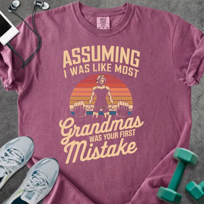 Berry t-shirt printed with "Assuming I Was Like Most Grandmas Was Your First Mistake" in white and gold, with a grandma lifting dumbbells graphic