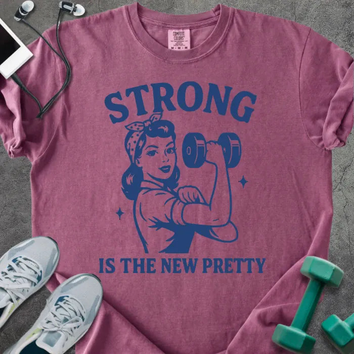 Berry t-shirt printed with "Strong is the New Pretty" in blue, with a Rosie the Riveter figure with a dumbbell