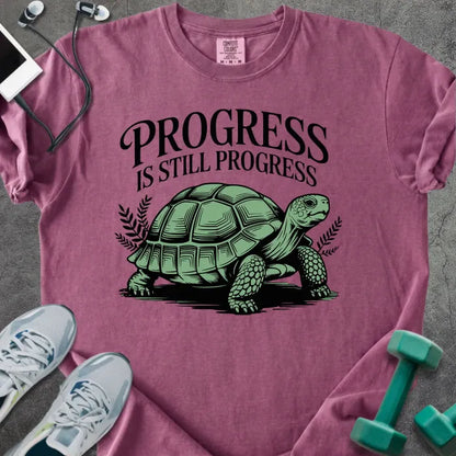 Berry t-shirt printed with "Progress is Still Progress" in green, with a turtle illustration and decorative leaves
