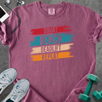 Berry t-shirt printed with "Squat Bench Deadlift Repeat" in red, teal, tan, orange, with red, teal, tan, and orange paint-stroke bands behind the words
