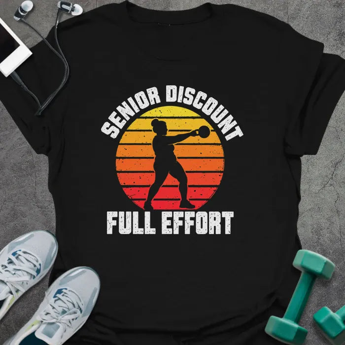 Black t-shirt printed with "SENIOR DISCOUNT, FULL EFFORT" in white, with a woman swinging a kettlebell against a retro yellow, orange and red sunset