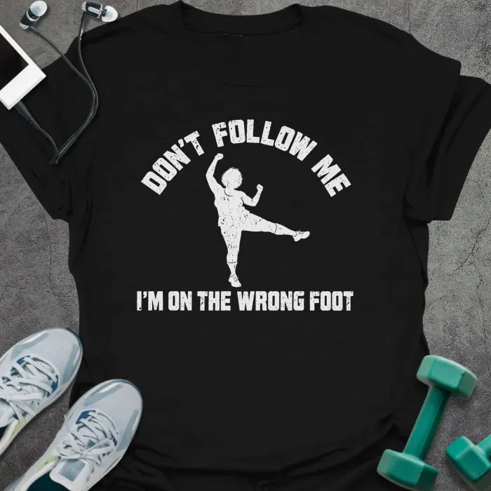 Black t-shirt printed with "DON'T FOLLOW ME, I'M ON THE WRONG FOOT" in white, with an older woman doing an aerobics kick