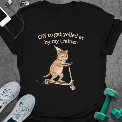 Black t-shirt printed with "Off to get yelled at by my trainer" in tan, white, with a cat on a scooter
