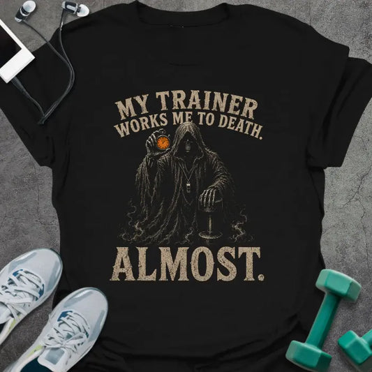 Black t-shirt printed with "MY TRAINER WORKS ME TO DEATH. ALMOST." in tan, with grim reaper graphic