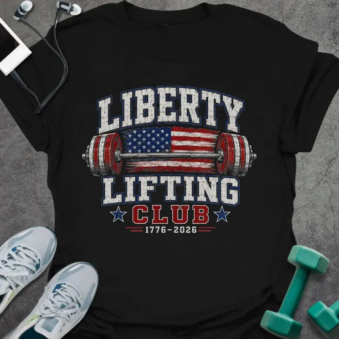 Black t-shirt printed with "Liberty Lifting Club 1776-2026" in white, red, and blue, with a stars-and-stripes barbell and eagle