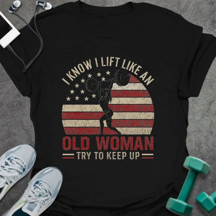 Black t-shirt printed with "I Know I Lift Like an Old Woman Try to Keep Up" in red and white, with a flexing woman silhouette and American flag kettlebell