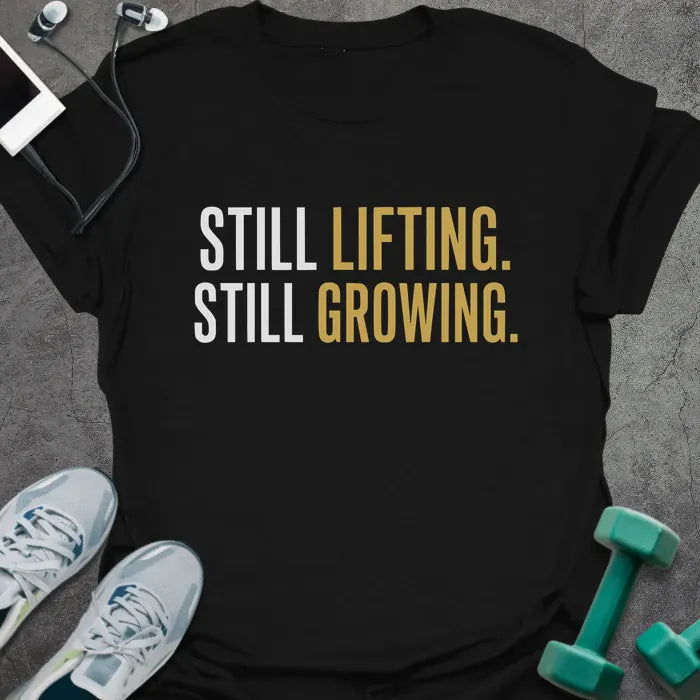 Black t-shirt printed with "Still Lifting. Still Growing." in white and gold