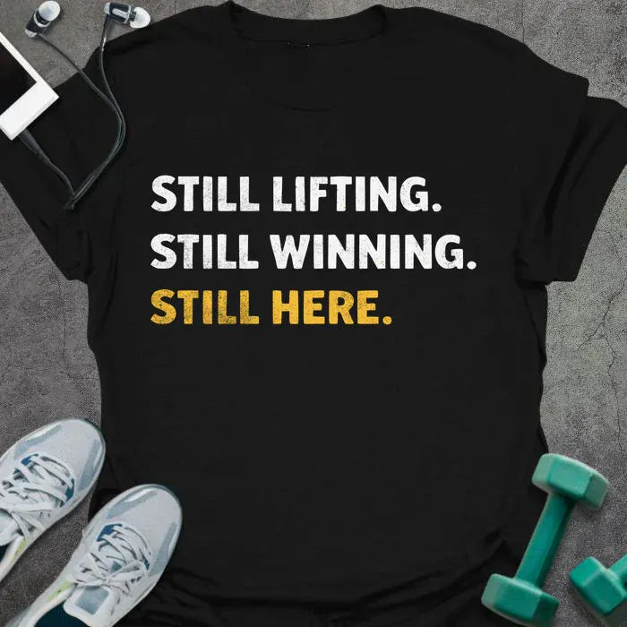 Black t-shirt printed with "Still Lifting. Still Winning. Still Here." in white and yellow
