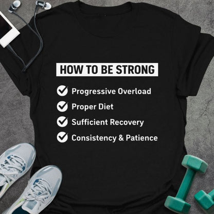 Black t-shirt printed with "HOW TO BE STRONG ✓ Progressive Overload ✓ Proper Diet ✓ Sufficient Recovery ✓ Consistency & Patience" in white