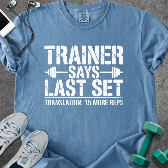 Blue jean t-shirt printed with "Trainer Says Last Set Translation: 15 More Reps" in white, with a barbell graphic