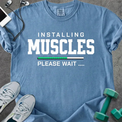Blue jean t-shirt printed with "Installing Muscles Please Wait ...." in white and multicolor, with a loading bar