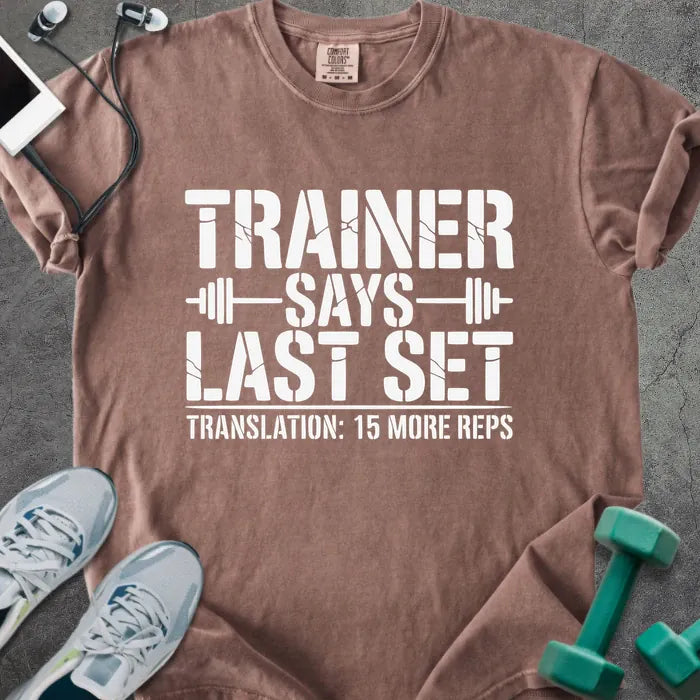 Espresso t-shirt printed with "Trainer Says Last Set Translation: 15 More Reps" in white, with a barbell graphic