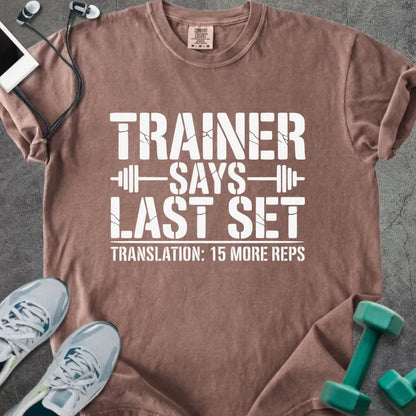 Espresso t-shirt printed with "Trainer Says Last Set Translation: 15 More Reps" in white, with a barbell graphic