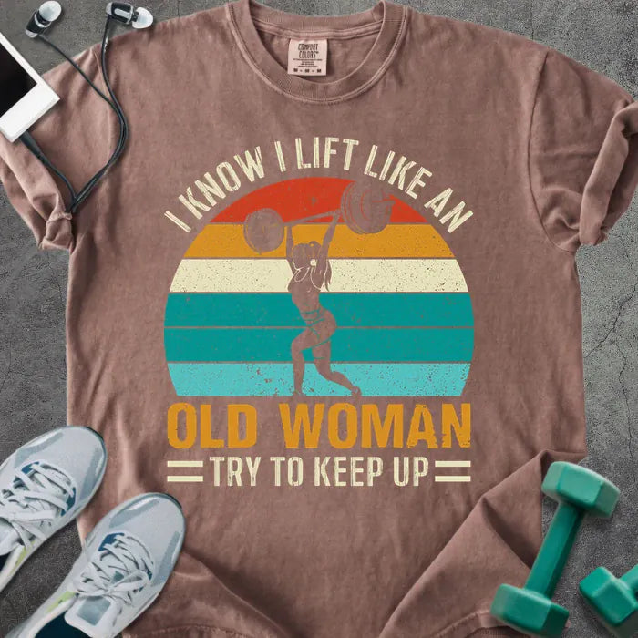 Espresso t-shirt printed with "I Know I Lift Like an Old Woman Try to Keep Up" in orange and multicolor, with a lifting silhouette and rainbow sunset