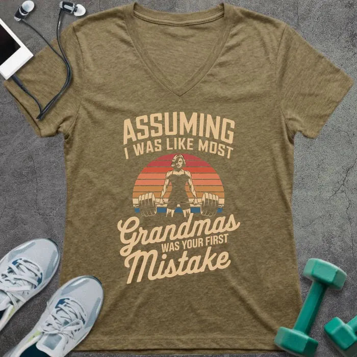 Heather olive t-shirt printed with "ASSUMING I WAS LIKE MOST Grandmas WAS YOUR FIRST Mistake" in cream, orange, red, black, with a muscular woman silhouette deadlifting over a retro sunset